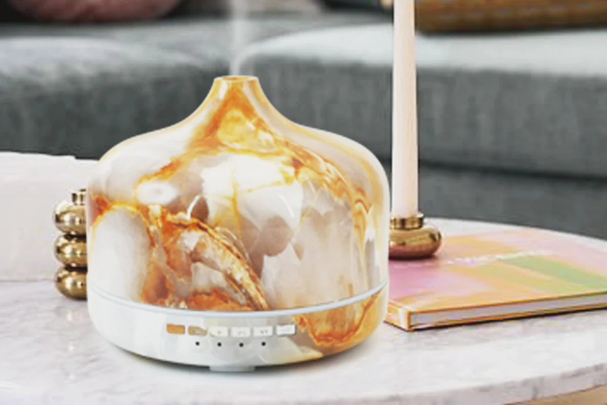 Marbled-glass ultrasonic aroma diffuser on a marble coffee table beside a lit taper candle
