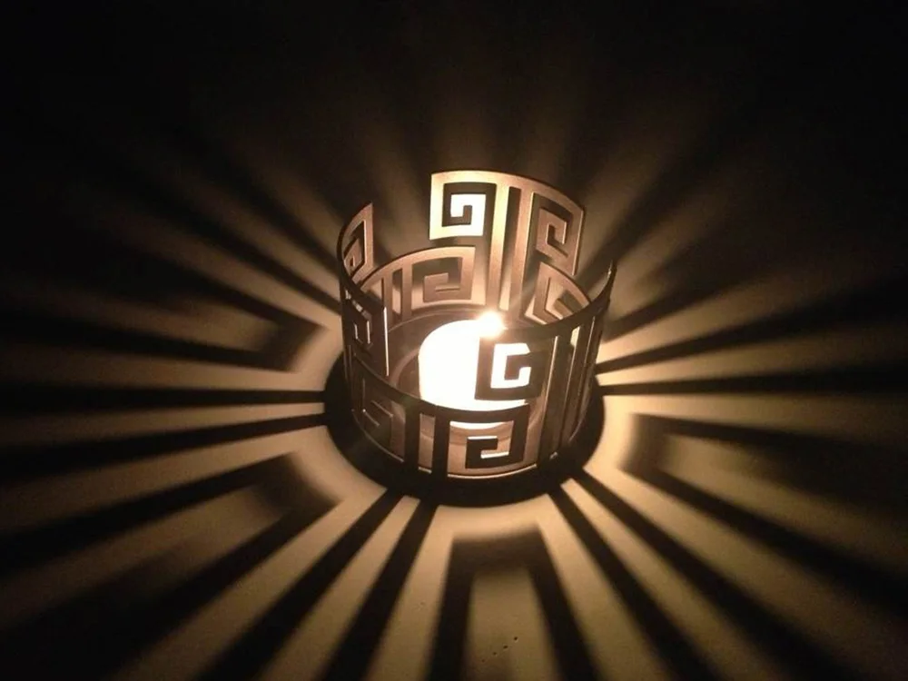 Metal Greek-key tealight holder casting a pattern of light
