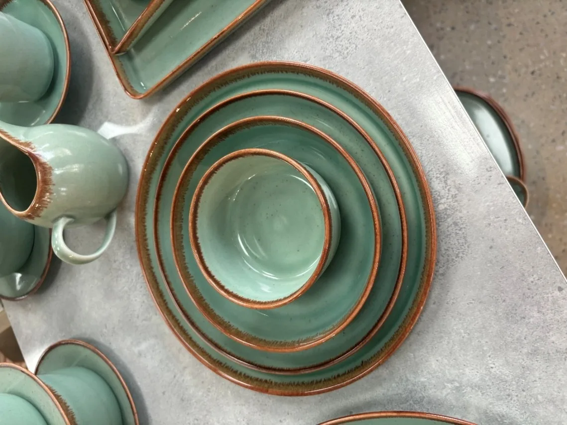 Green reactive-glaze stoneware dinnerware with a brown rim, nested